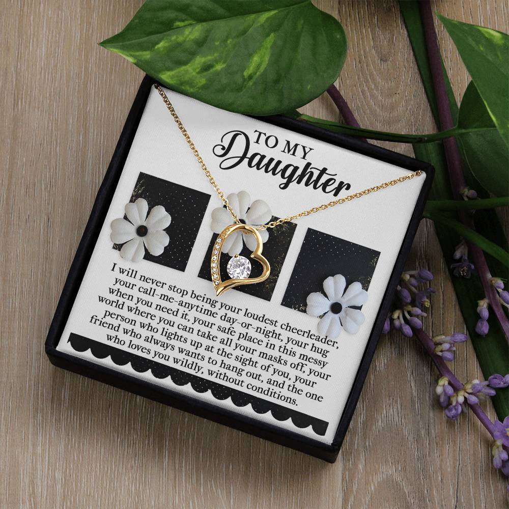 The Daughter-Loudest Cheerleader - Forever Love Necklace, showcasing a heart and crystal pendant with a white gold finish, is gracefully presented in a box that features a heartfelt printed message for your daughter. Nestled among decorative flowers and leaves on a wooden surface, it gleams beautifully with cubic zirconia accents.