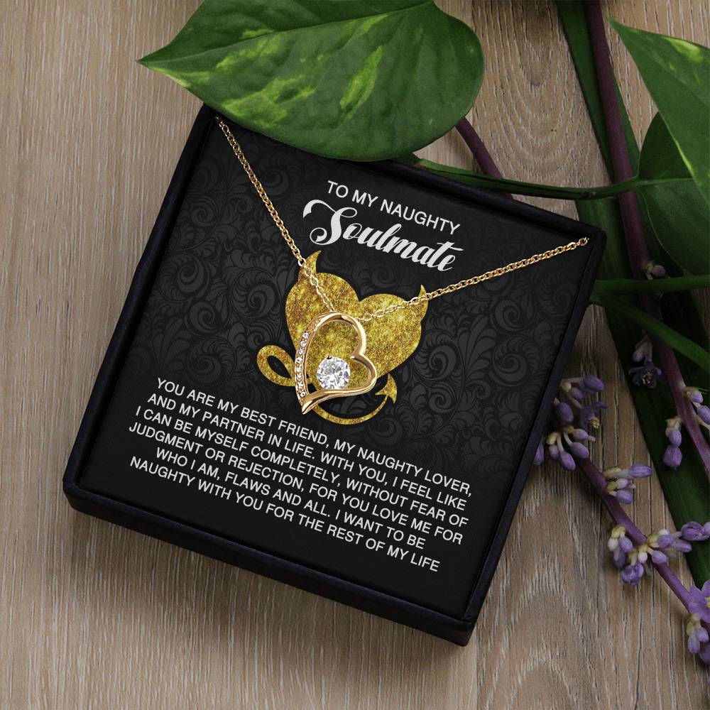 The Soulmate-Naughty With You - Forever Love Necklace, featuring a heart pendant with a cubic zirconia stone, is elegantly displayed on a black jewelry box. This box includes a heartfelt message for a "naughty soulmate," framed by green leaves and purple flowers.