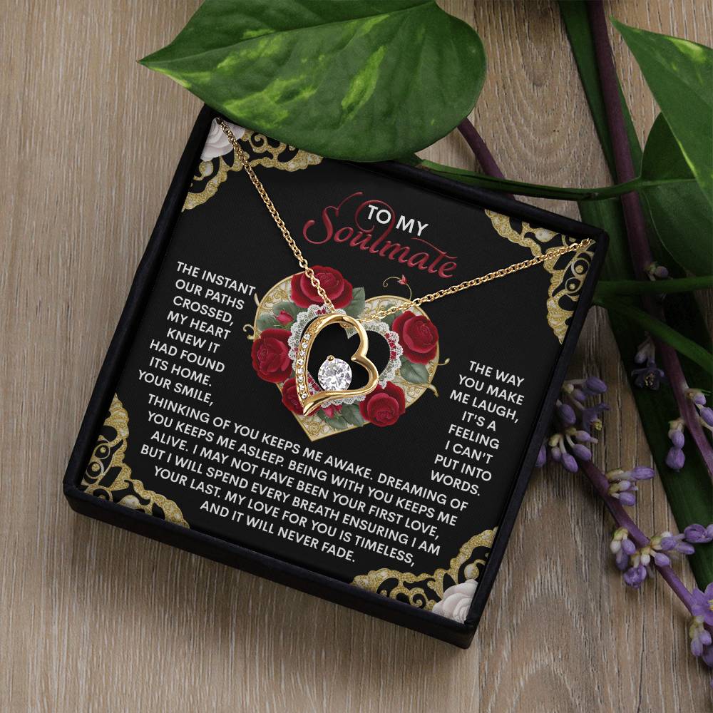 A heart-shaped pendant necklace elegantly finished in white gold features a rose design. In a box, it includes a card with a romantic message to a soulmate, resting on wood surrounded by greenery and purple flowers—capturing the essence of the Soulmate-Never Fade - Forever Love Necklace.