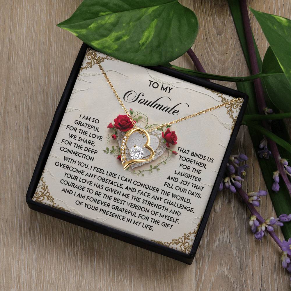 The Soulmate-Our Days - Forever Love Necklace, with a white gold finish and CZ crystal pendant, features a gold heart adorned with roses and diamonds on a card reading "To My Soulmate..." It is elegantly presented in a black box surrounded by lush leaves and flowers.