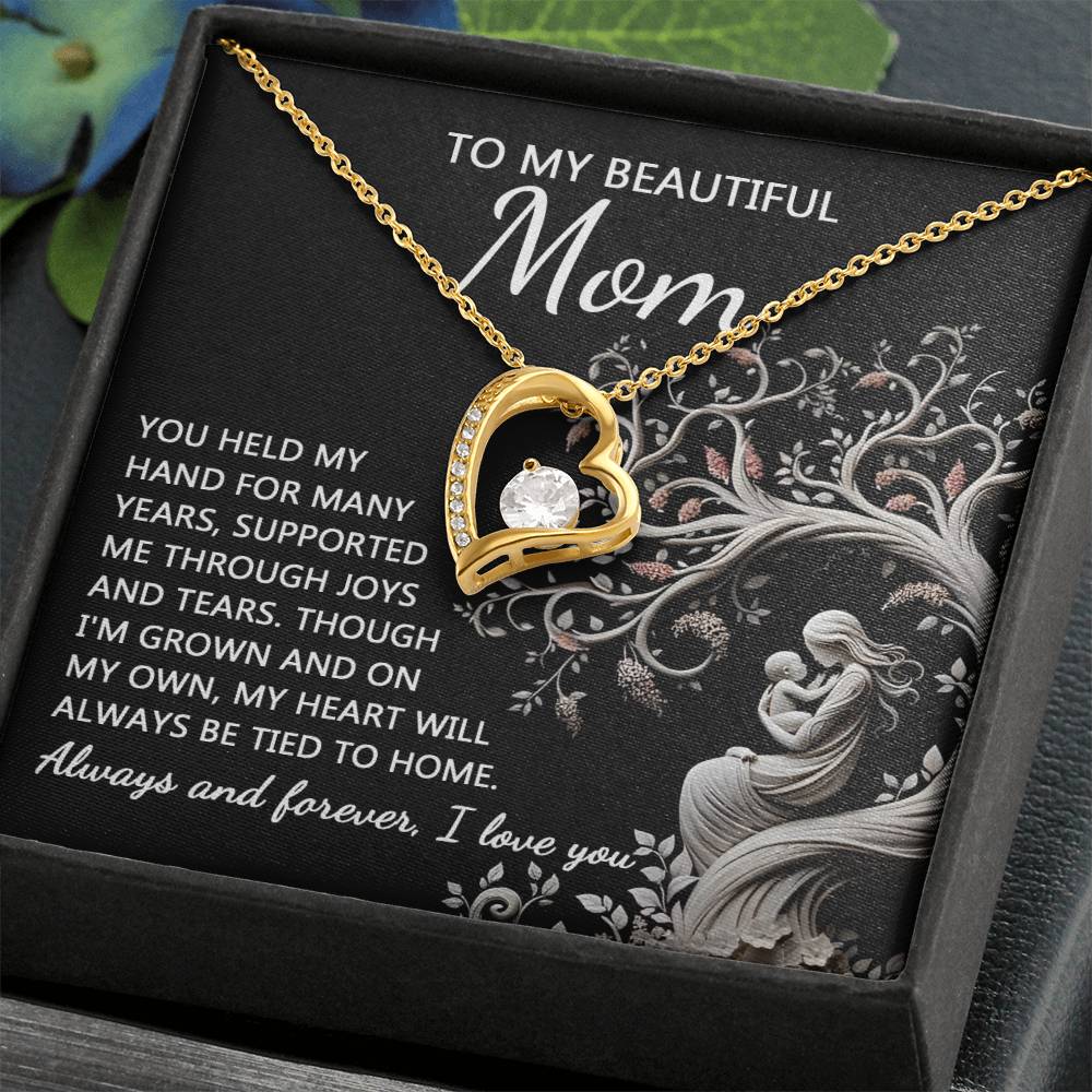 A gold heart-shaped "To Mom, On My Own - Forever Love Necklace" with a dazzling cubic zirconia stone at its center is showcased in an open box. The box features a personalized message dedicated to a mother, expressing gratitude, love, and an everlasting connection.