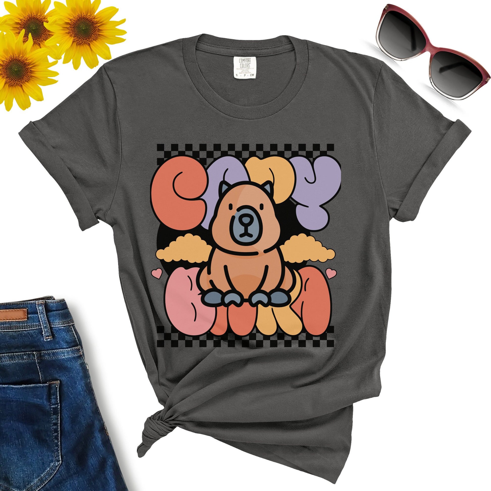 Cute Capybara T-shirt featuring a cartoon dog surrounded by colorful letters. This premium cotton t-shirt is styled with blue jeans, sunglasses, and yellow flowers. Golden Value SG ensures both comfort and style.