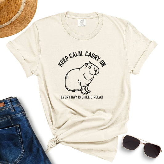 A white Crewneck T-Shirt for Women & Men featuring a graphic of a capybara and the text "KEEP CALM. CARRY ON. EVERY DAY IS CHILL & RELAX." Surrounding the Keep Calm Carry On Funny Capybara Shirt That Go Hard are a straw hat, blue jeans, and sunglasses – making it the perfect capybara-themed gift for any casual outfit lover.