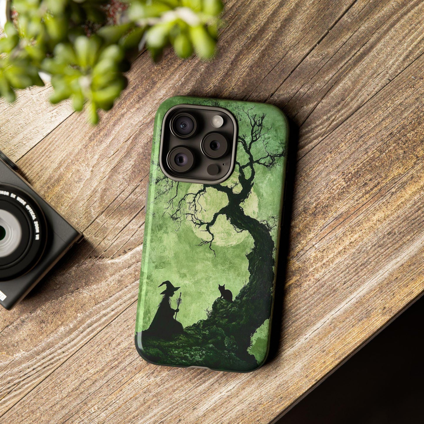 The Spooky Witch With Black Cat Phone Case is a perfect Halloween accessory for cat enthusiasts. Featuring a green and black design that displays an eerie silhouette of a witch with her black cat near a twisted tree, it rests charmingly on your wooden surface, adding an enchanting touch beside your camera. Ideal as a witchcraft cat case or Halloween gift, it's compatible with iPhone 15/14/13, Samsung S24 Galaxy, and Pixel models.