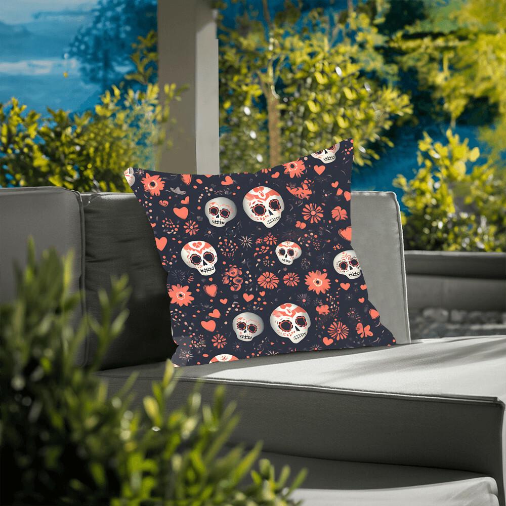 A Day of the Dead Mexican Skull Pillow, showcasing sugar skull patterns with hearts and flowers against a dark backdrop, is placed on an outdoor sofa, enhancing the space with goth home decor vibes. Green foliage can be seen in the background.