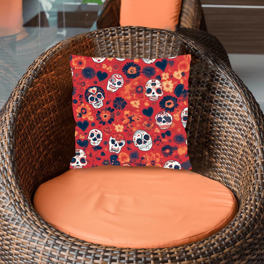 A wicker chair with an orange cushion and a striking Day of the Dead Mexican Skull Pillow, designed for Halloween or Día de los Muertos decor, featuring intricate skull art interwoven with red, black, and white floral patterns.