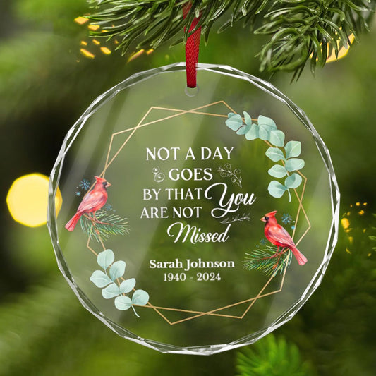 The Personalized Cardinal Memorial Christmas Ornament by Golden Value SG, adorned with cardinals and greenery and inscribed with the text &quot;Not a day goes by that you are not missed, Sarah Johnson 1940-2024,&quot; is elegantly displayed on a tree branch.