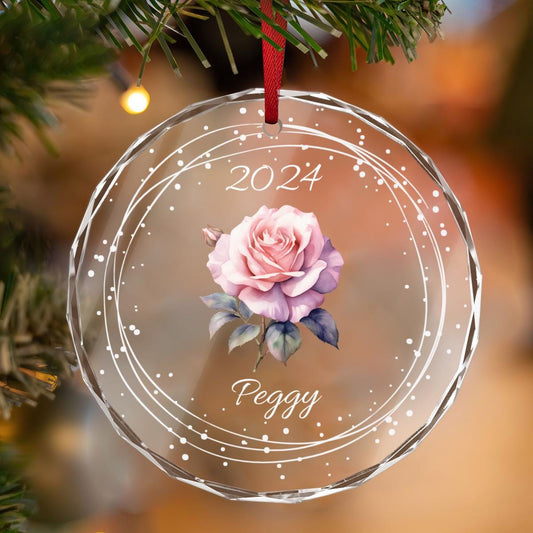 A Personalized Birth Month Flower Ornament by Golden Value SG, featuring a round glass design with a pink rose illustration, the year &quot;2024,&quot; and the custom name &quot;Peggy&quot; in white text, elegantly hanging from a tree.