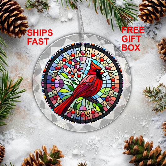 A Red Cardinal GLASS Ornament by Golden Value SG is hanging on a Christmas tree. The circular design features a lifelike cardinal perched on a branch, surrounded by a mosaic of floral patterns in greens, blues, pinks, and yellows.