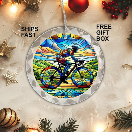 A Golden Value SG Cyclist GLASS Ornament featuring a stained glass design shows a cyclist riding through a vibrant landscape, set against white background and holiday lights.