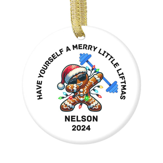 A white Merry Liftmas Weightlifting Ceramic Ornament featuring a playful gingerbread man in a Santa hat & sunglasses, & lifting a barbell adorned with Christmas light bulbs. The phrase &quot;HAVE YOURSELF A MERRY LITTLE LIFTMAS&quot; and Nelson 2024.