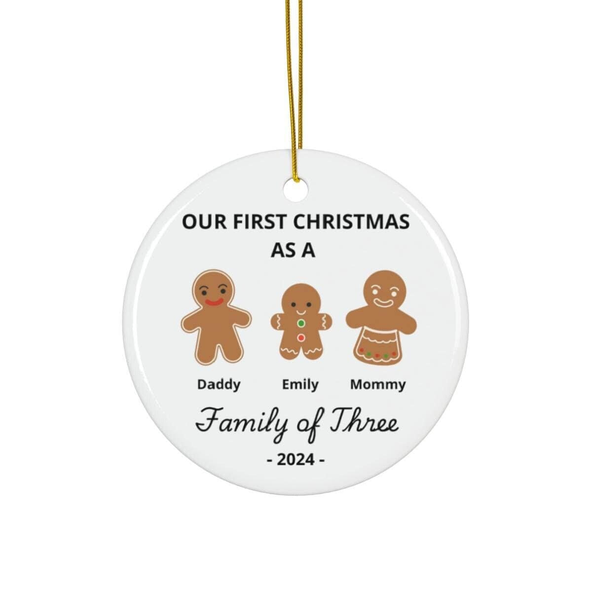 Round Christmas ornament featuring gingerbread characters labeled Daddy, Emily, and Mommy. The inscription says: "Our First Christmas as a Family of Three - 2024." This Personalized Family Of Three Christmas Ornament is an ideal keepsake for celebrating baby's first Xmas as part of your joyful trio.