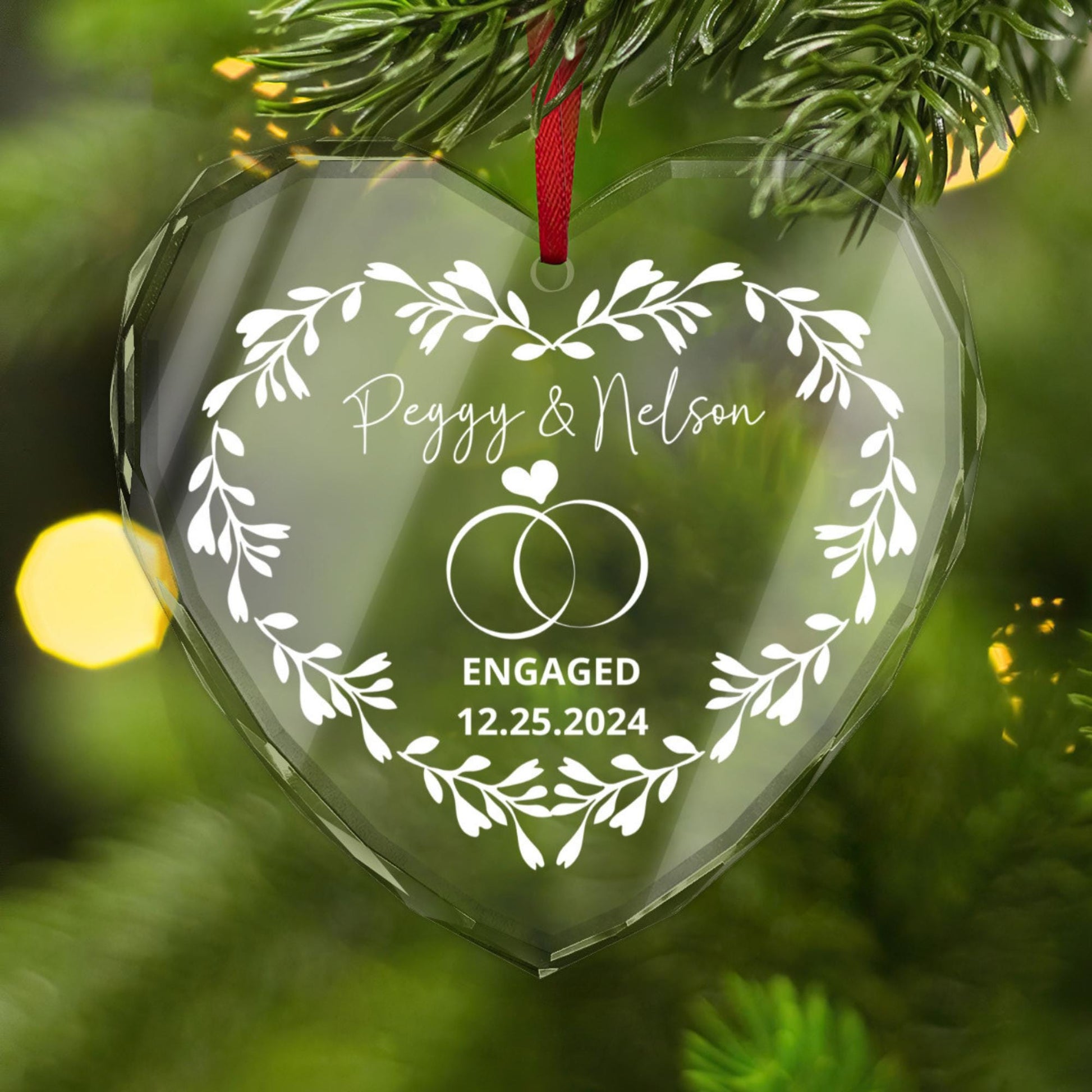 The Golden Value SG Personalized Engagement CRYSTAL GLASS Ornament features a heart shape with &quot;Peggy & Nelson Engaged 12.25.2024&quot; and two rings design, hanging on a Christmas tree.