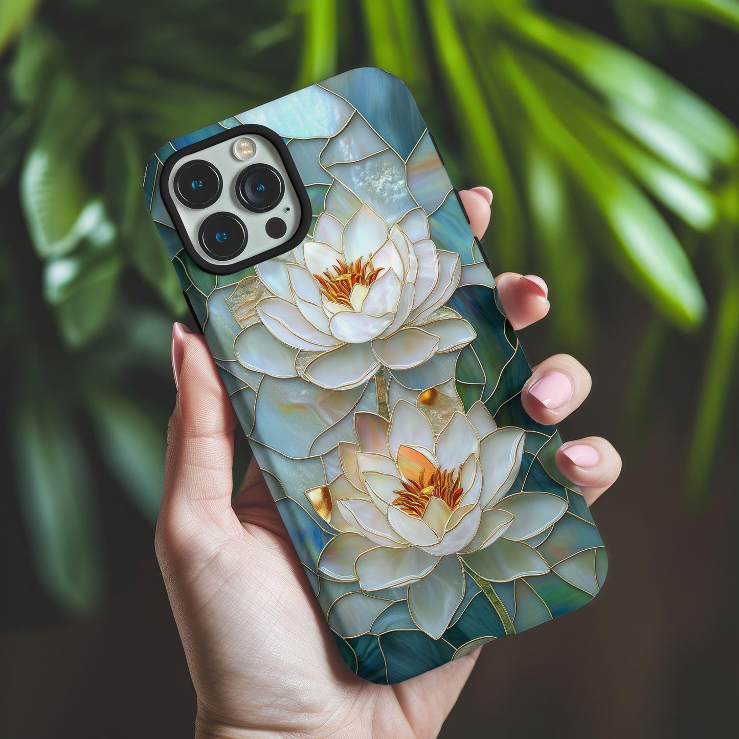 A hand holds the Elegant Stained Glass Lotus Phone Case by Golden Value SG featuring two luminous white lotus flowers with golden outlines and vibrant orange centers. The flowers are set against a mosaic of abstract blue and green shapes, evoking a tranquil water garden scene, perfect for a serene floral art piece. Green foliage is softly blurred in the background.