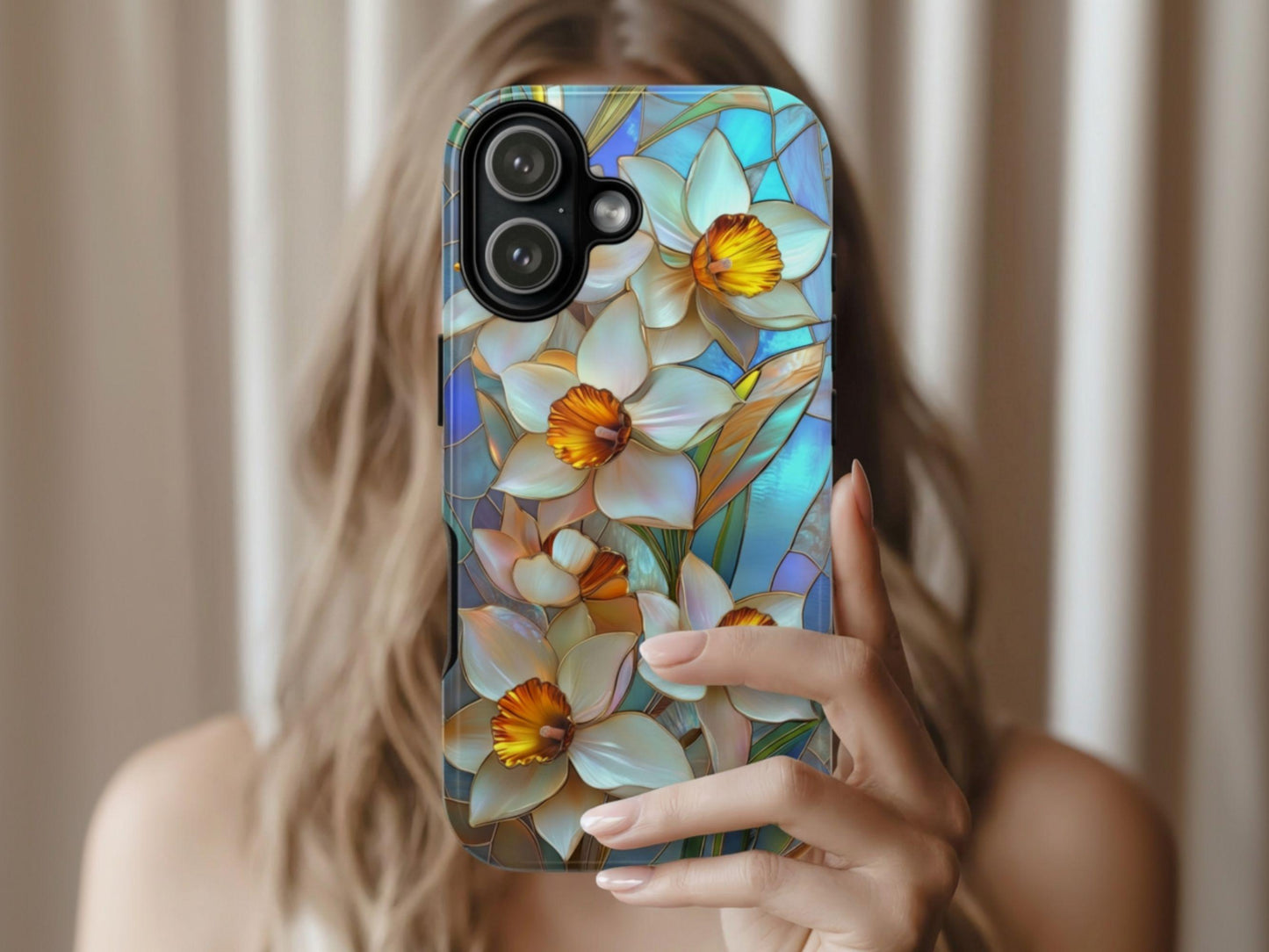 A woman with light brown hair holds up a Stained Glass Daffodil Phone Case Golden Value SG featuring elegant white daffodils with vibrant yellow centers and green leaves against a mosaic-style blue and teal background. This floral design captures the delicate beauty of spring flowers in a colorful, art-inspired pattern, perfect for adding a touch of artistic charm to your device.