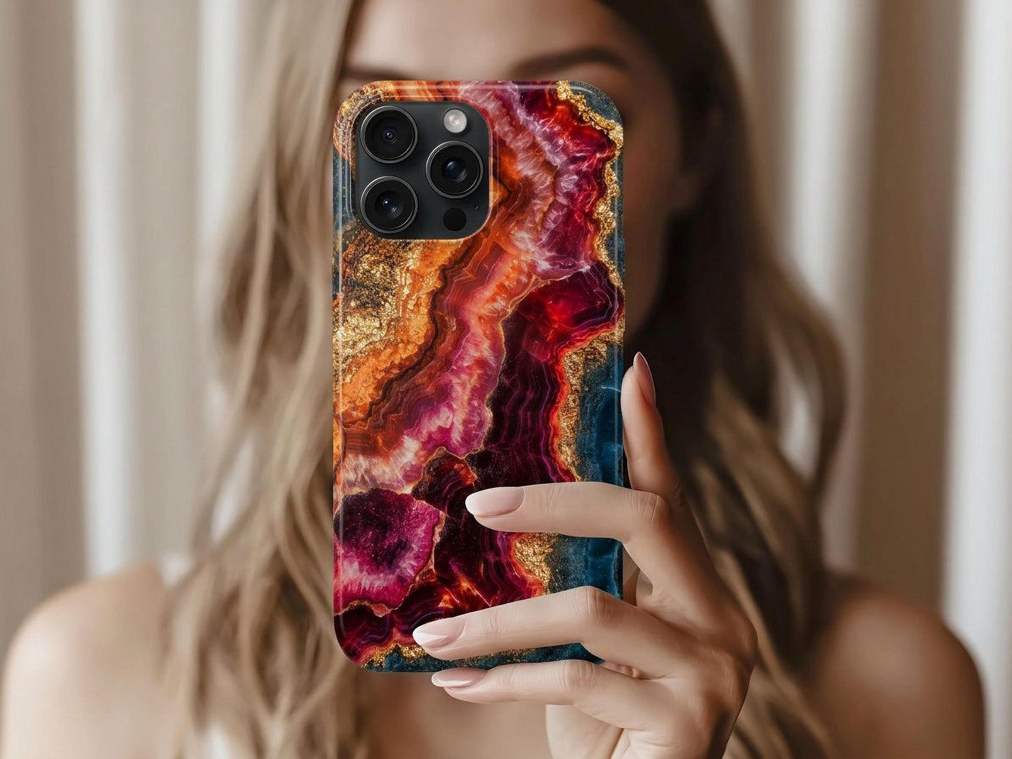 A woman with light brown hair holds up the Elegant Ruby Crystal Phone Case by Golden Value SG features swirling deep red, purple, orange, and gold bands in a marbled geode pattern with glittering metallic highlights along jagged edges.