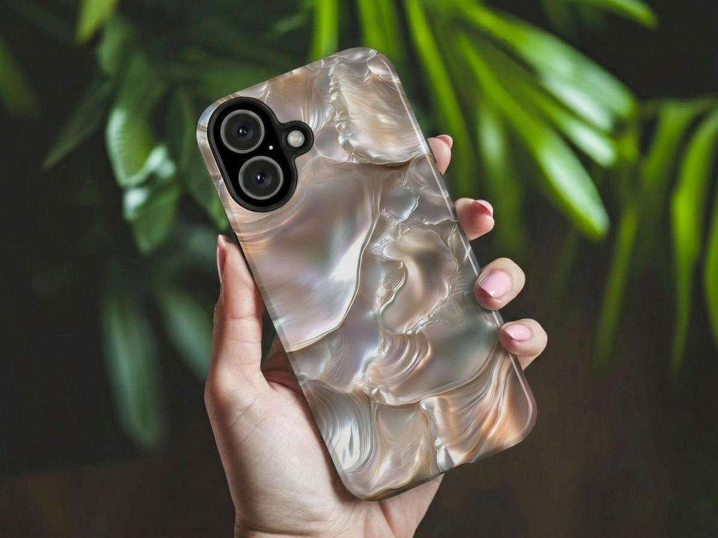 A hand holds the June Birthstone Mother of Pearl Phone Case by Golden Value SG features iridescent layers with smooth, pearly surfaces in soft white, gold, pink, and blue hues that reflect light in wavy, fluid patterns. Green foliage is softly blurred in the background.