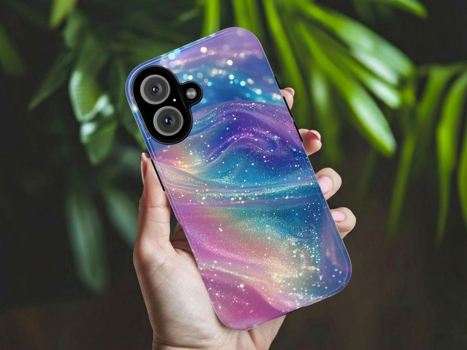 A manicured hand holds the Pastel Rainbow Phone Case by Golden Value SG, showcasing swirls of blue, purple, and pink with sparkling glitter. The background features softly blurred green leaves.