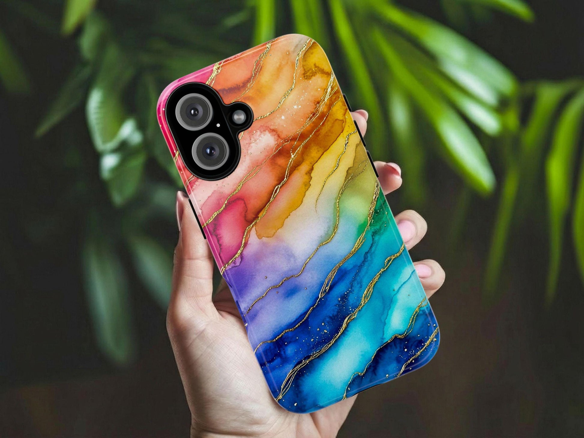 A hand holds the Golden Value SG’s Rainbow Ink Pattern Aesthetic Phone Case showcasing a mesmerizing marbling effect with shades transitioning from pink and purple to blue and teal. Golden veins meander through the colors, adding a touch of luxury and sophistication., with blurred green leaves in the background.