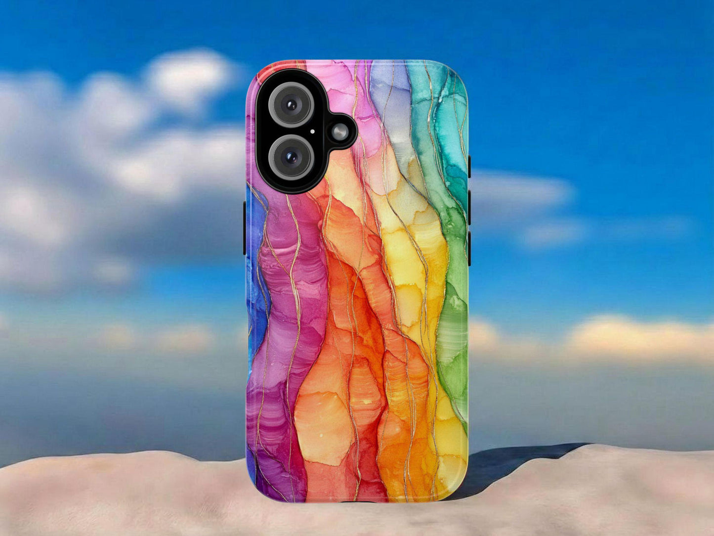 The Golden Value SG Rainbow Phone Case, featuring a colorful wavy abstract design, stands upright on a smooth pale surface against a bright blue sky with white clouds, creating a lively and vibrant scene.