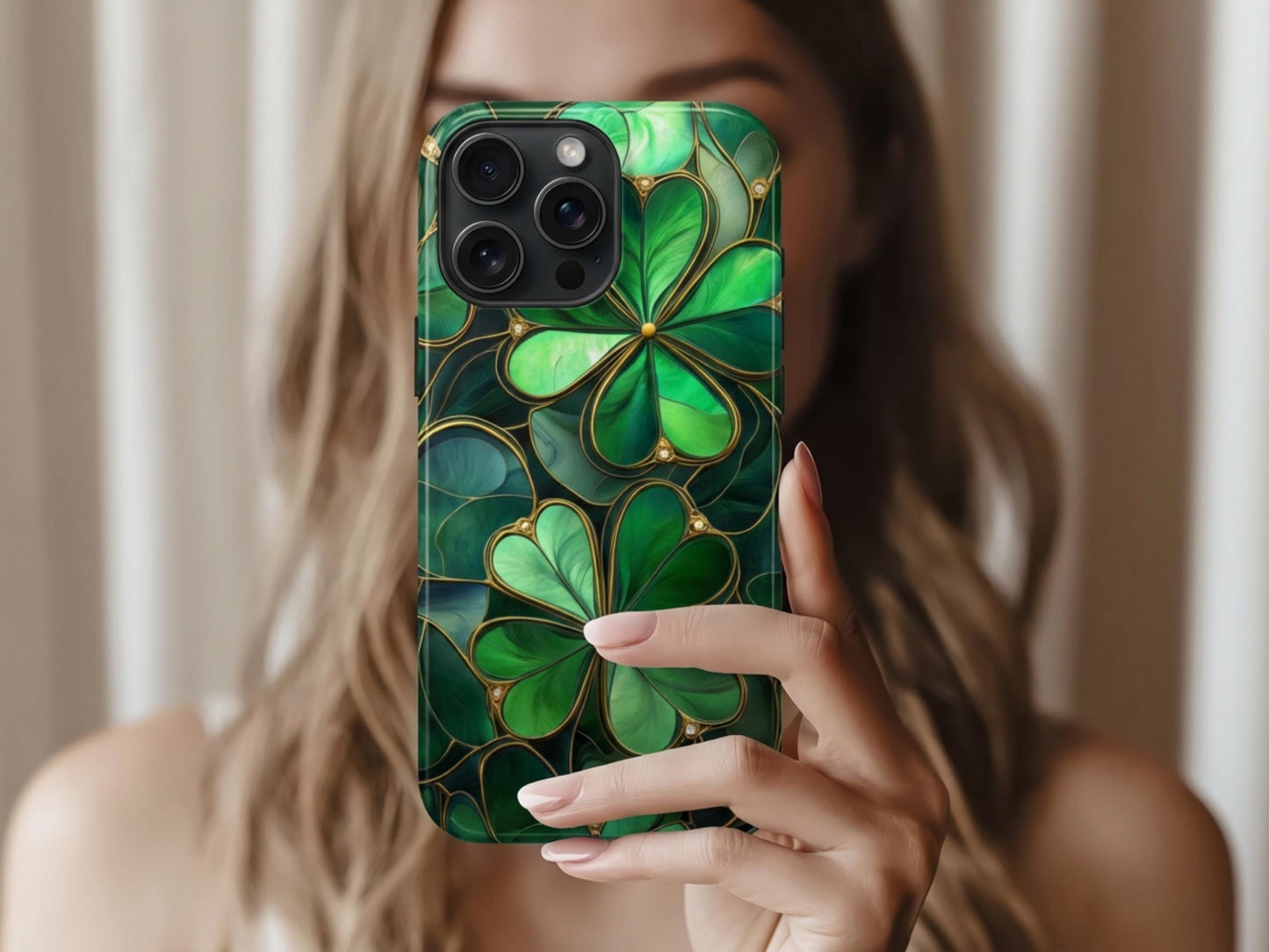 A woman with light brown hair holds up a luxurious Golden Value SG Shamrock Phone Case with a rich green stained glass Shamrock clover leaf with intricate gold outlines and subtle gemstone accents. The design showcases varying shades of green and dark blue, evoking elegance and natural beauty in a sophisticated artistic style.