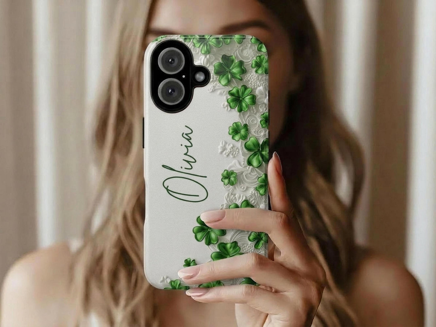 A woman with light brown hair holds up a Personalized Custom Shamrock Phone Case by Golden Value SG with vibrant green glossy clovers and subtle embossed white floral patterns. The name "Olivia" is elegantly written in cursive green font, combining nature-inspired aesthetics with a sophisticated personalized touch.