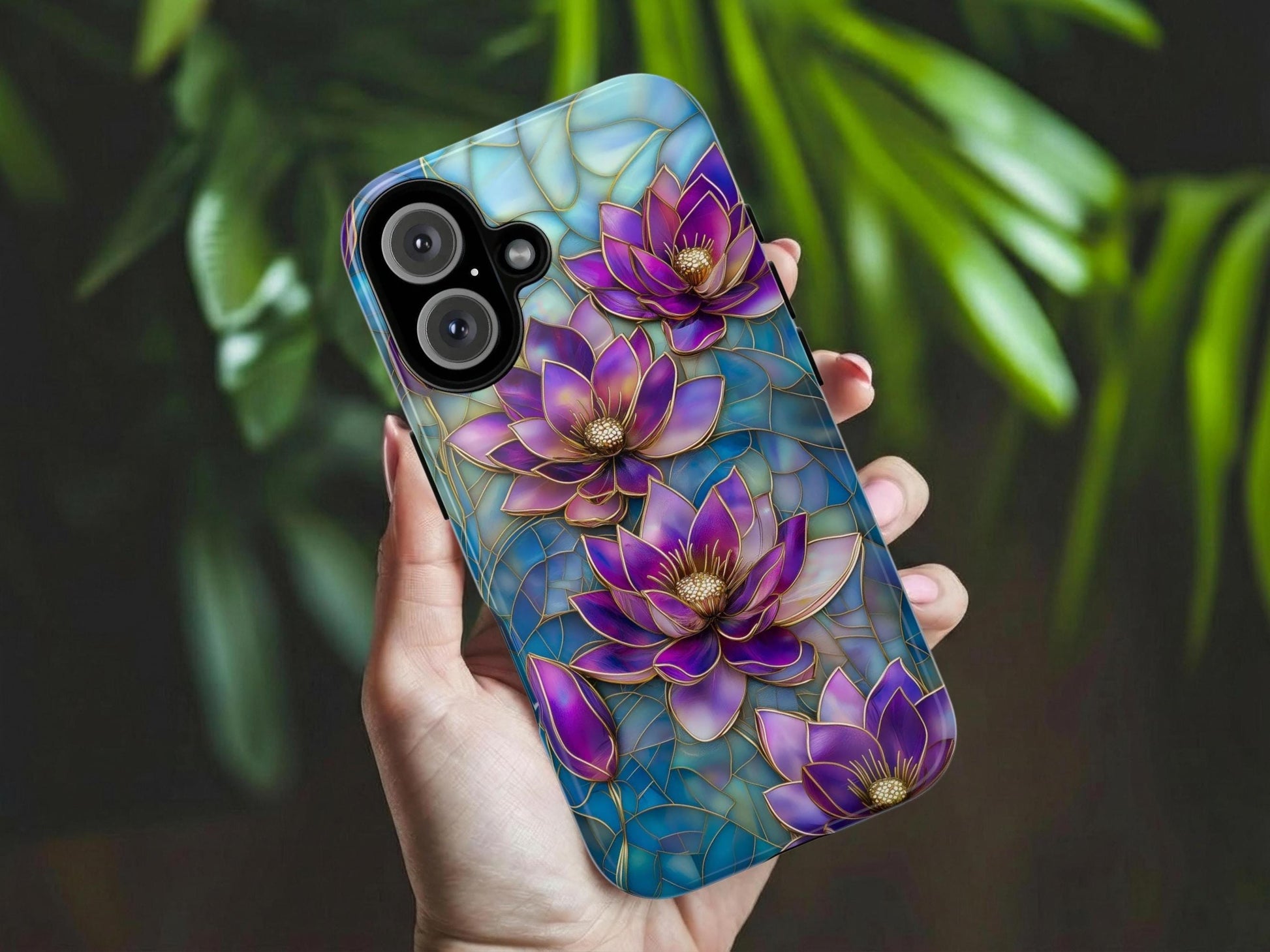 A hand holds the Purple Lotus Phone Case by Golden Value SG features stunning purple and violet lotus flowers with intricate gold-outlined petals set against a luminous mosaic stained glass background in shades of blue and teal. Multiple blooms and buds are arranged across the design with golden stamens at each center, creating a rich, jewel-toned, luxurious floral art nouveau aesthetic. Green foliage is softly blurred in the background.