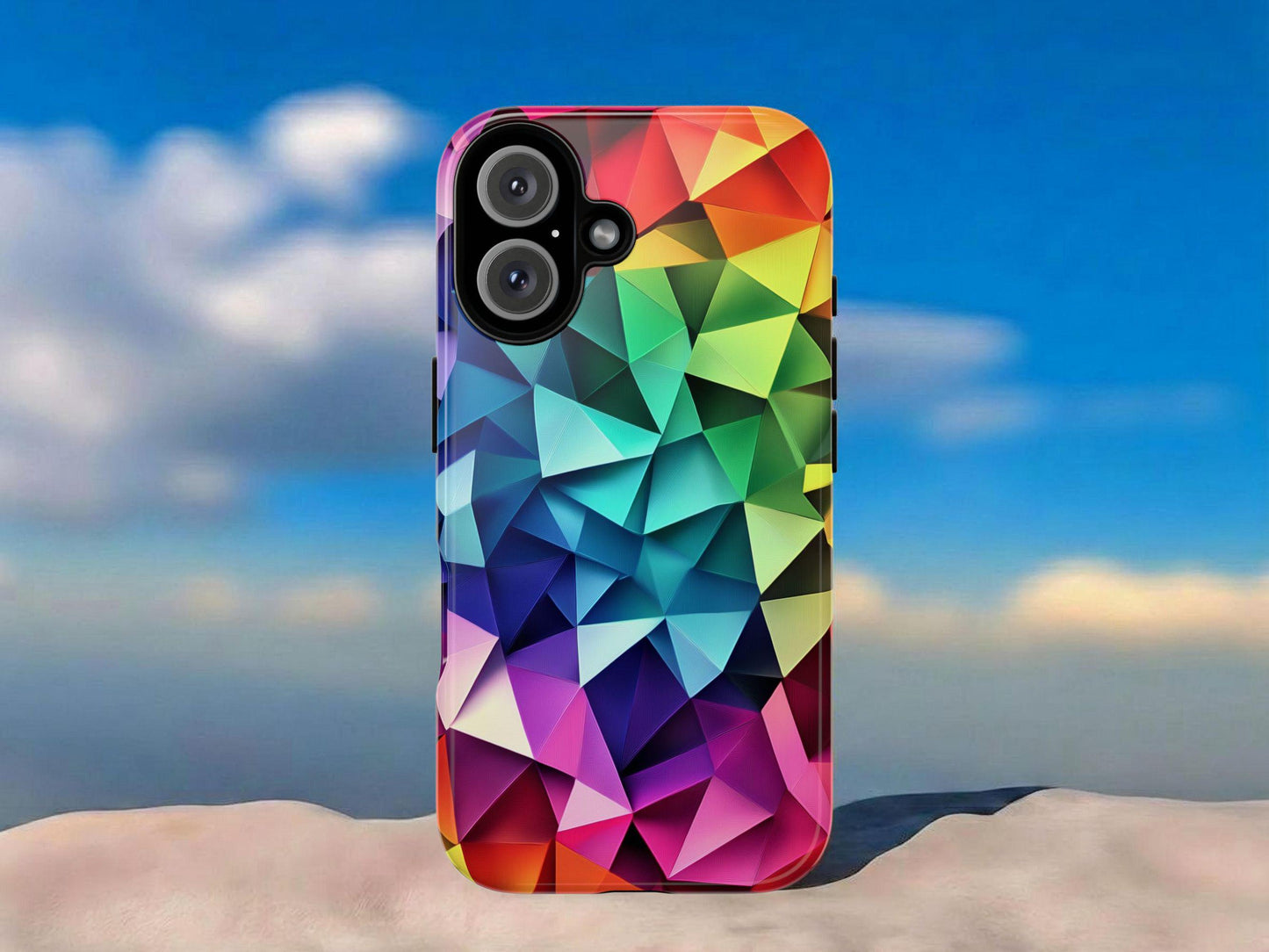 The Golden Value SG Geometric Rainbow Phone Case, featuring a vibrant 3D triangular pattern, displays upright on a smooth surface. Its colorful geometric design stands out against a backdrop of blue sky and scattered clouds.