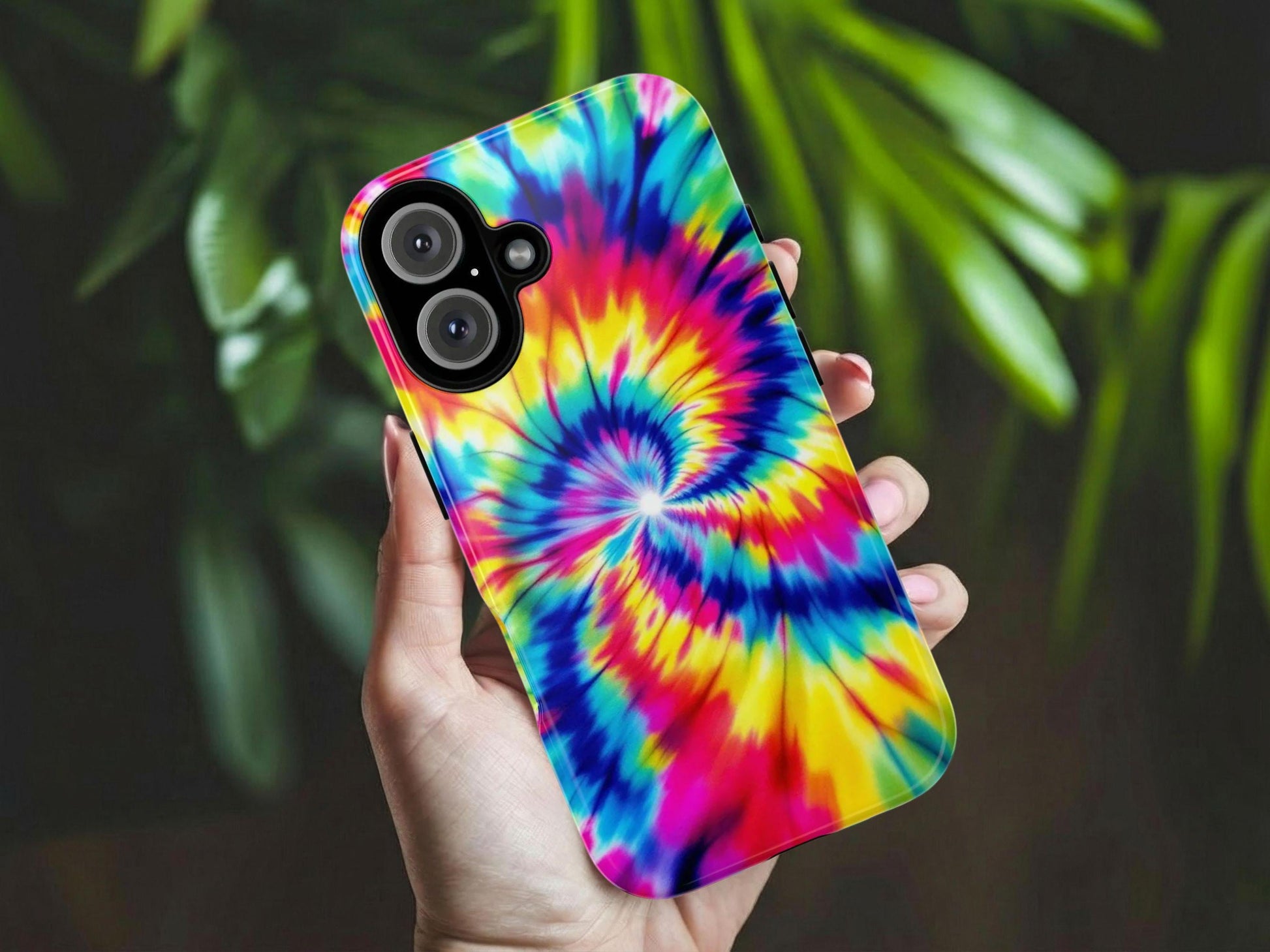 A hand holds the Groovy Tie Dye Phone Case by Golden Value SG features a vibrant spiral of yellow, blue, red, and green, creating a dynamic psychedelic effect. Green foliage is softly blurred in the background.