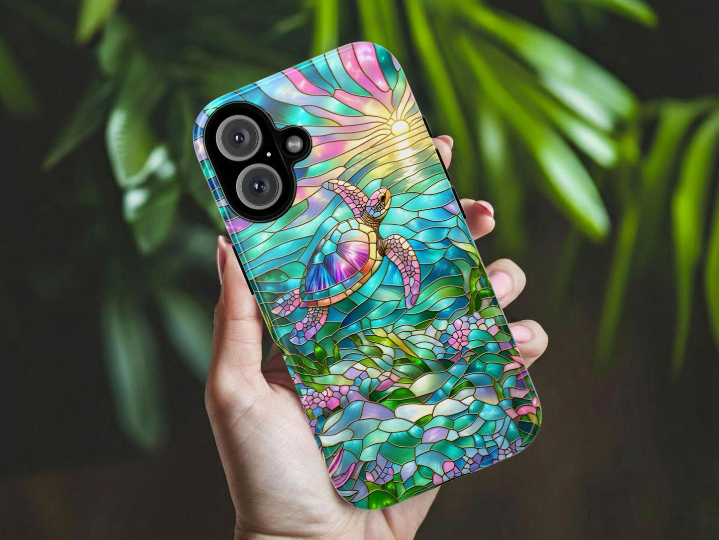 A hand holds a vibrant Sea Turtle Phone Case by Golden Value SG depicting an underwater scene with a colorful sea turtle swimming towards a radiant sun setting or rising on the horizon. The design features shimmering blue and green waters, pink and purple skies, and lush aquatic plants and flowers at the bottom, all outlined in golden lines. Green foliage is softly blurred in the background.