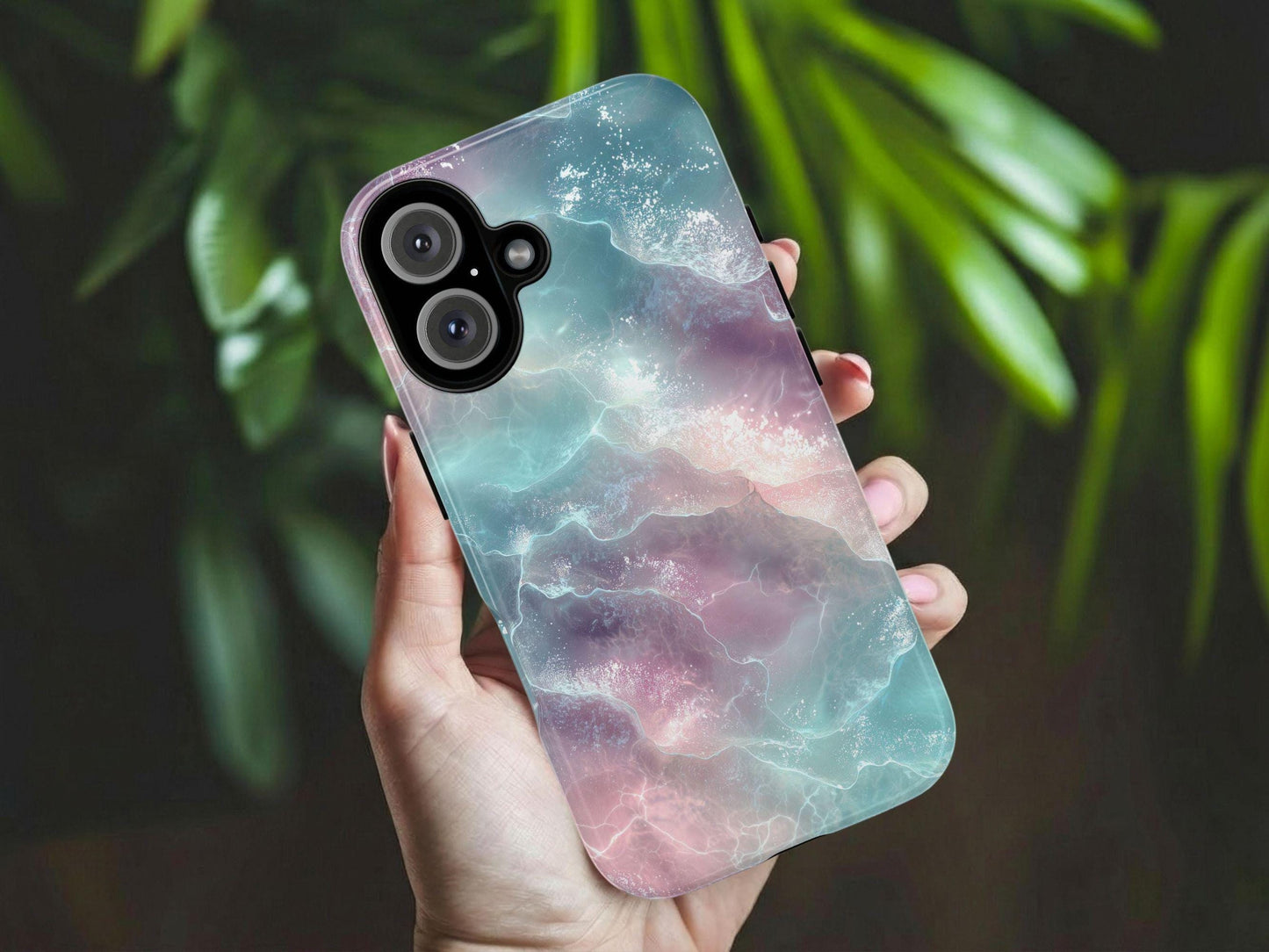 A hand holds the A Pastel Ocean Waves Phone Case  by Golden Value SG with shimmering, glassy waves in soft pastel pink, purple, and blue tones. Green foliage is softly blurred in the background. The design evokes a serene, surreal, and fantasy-like aquatic atmosphere with delicate highlights on the water's surface.