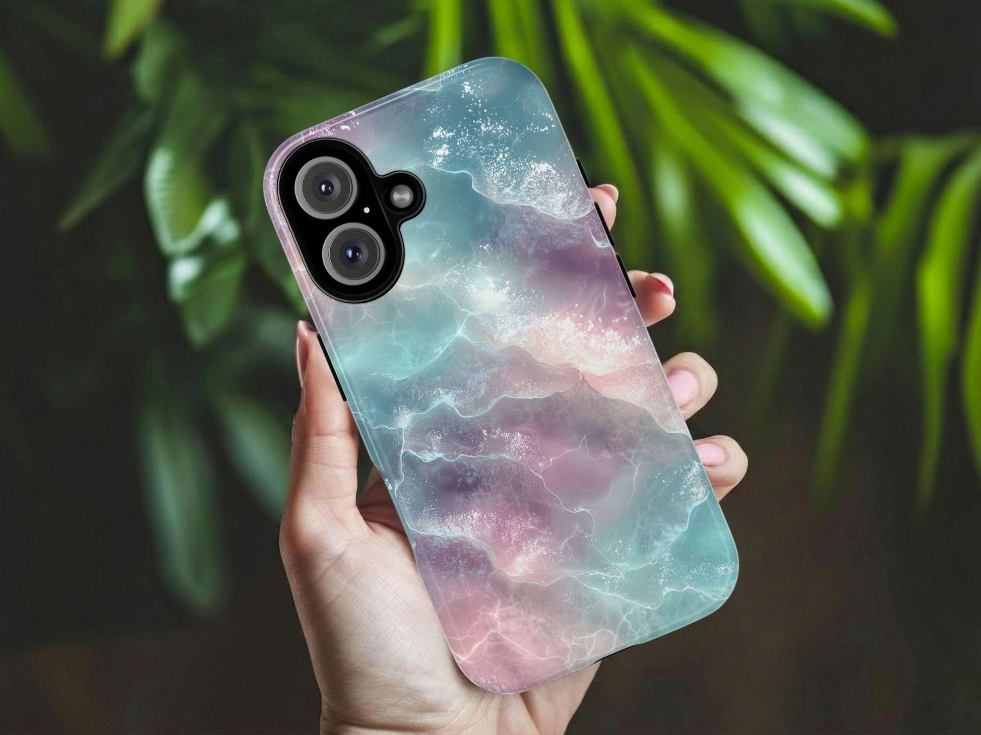 A hand holds the A Pastel Ocean Waves Phone Case  by Golden Value SG with shimmering, glassy waves in soft pastel pink, purple, and blue tones. Green foliage is softly blurred in the background. The design evokes a serene, surreal, and fantasy-like aquatic atmosphere with delicate highlights on the water's surface.