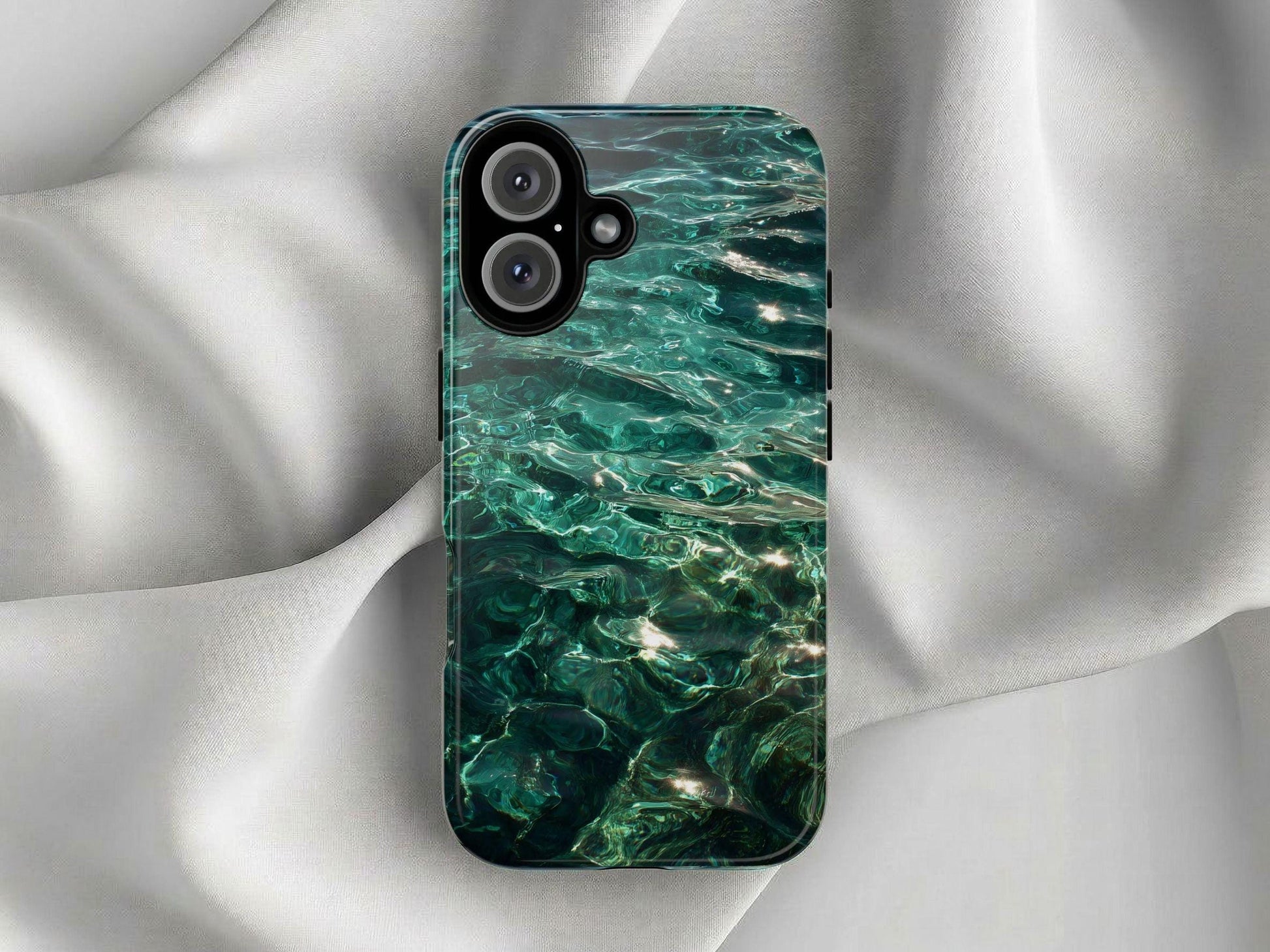 A vibrant Water Phone Case by Golden Value SG featuring emerald blue-green water surface with gentle ripples and shimmering sunlight reflections rests on smooth, light gray fabric, creating an elegant and soft backdrop for the smartphone. The clear water reveals abstract patterns and varying depths of color, creating a tranquil and pristine natural aesthetic.