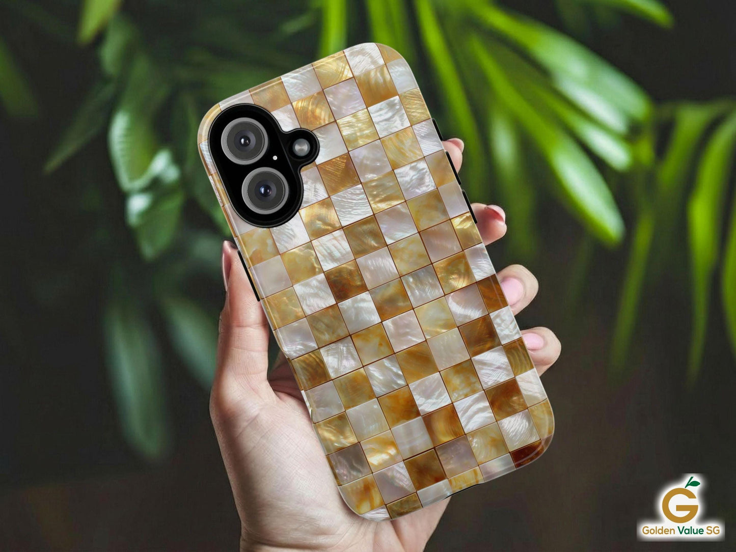 A hand holds the Trendy Gold Mosaic Phone Case by Golden Value SG featuring iridescent gold, white, and beige mosaic tiles with a shimmering, metallic mother-of-pearl effect. Perfect for elegant and unique style. Green foliage is softly blurred in the background.