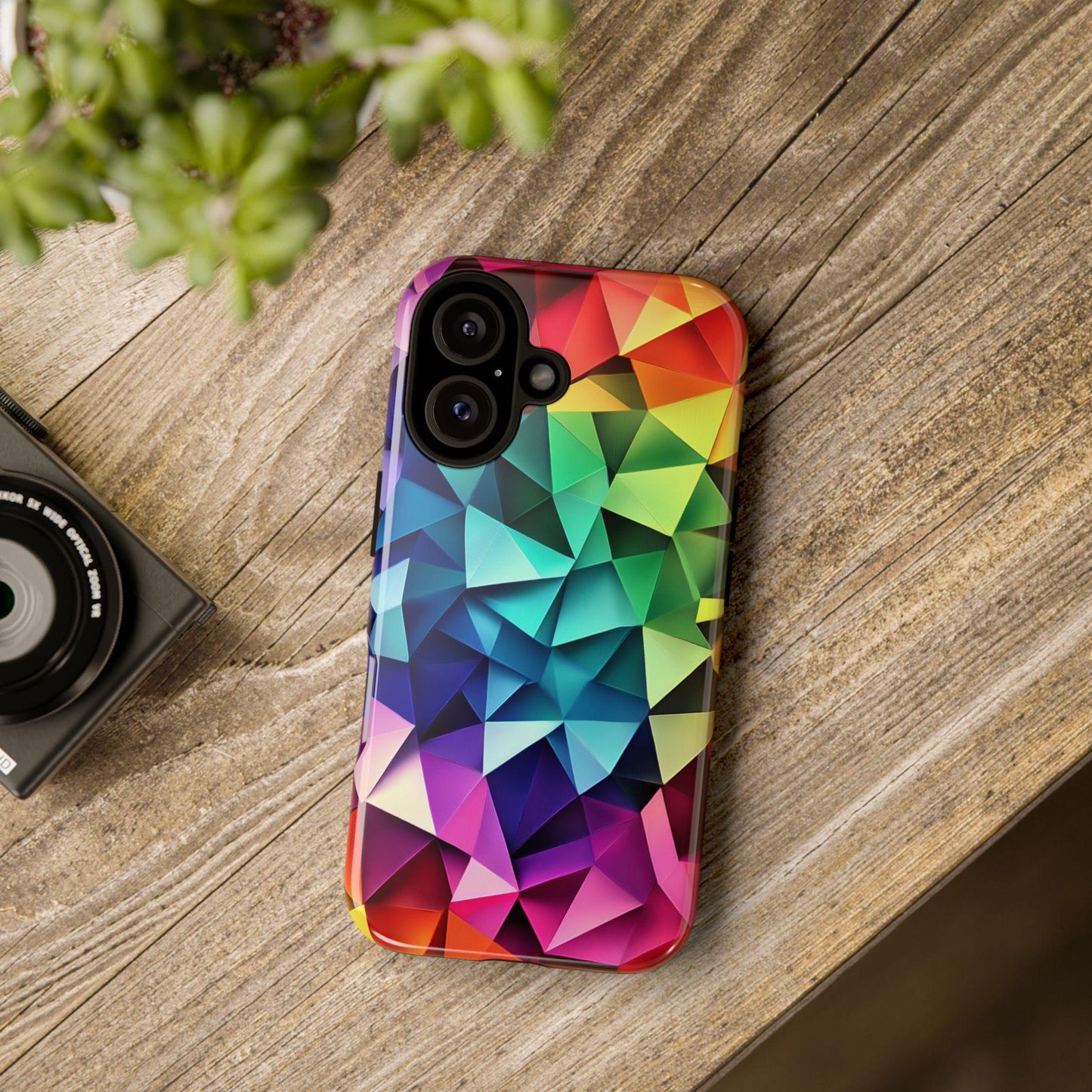 A colorful geometric mosaic phone case rests on a wooden surface next to a camera lens.
