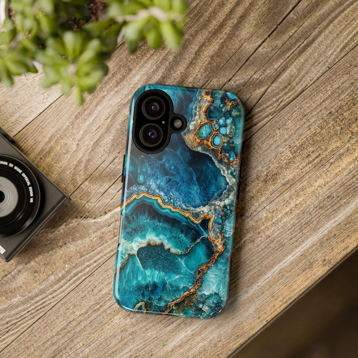 The turquoise geode design phone case lies flat on a wooden surface next to a camera.