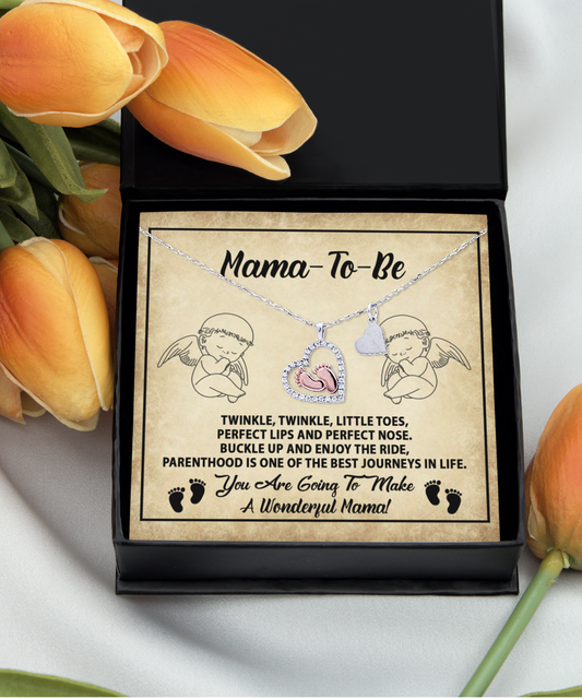 A gift box with a [Almost Sold Out] To Mama To Be, Enjoy The Ride - Baby Feet Necklace charm next to tulip flowers on a white surface.