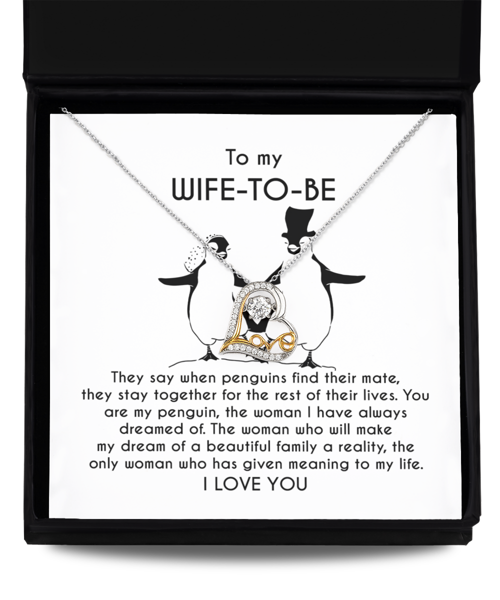 A silver heart-shaped necklace with an intertwined 14k gold plated heart centerpiece sits on a message card inside a black box. The card reads: "To my WIFE-TO-BE, I LOVE YOU" with a monologue about love and penguins. This is the Wife-to-be-My Penguin - Love Dancing Necklace.