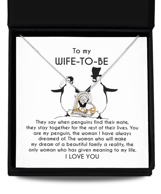 A silver heart-shaped necklace with an intertwined 14k gold plated heart centerpiece sits on a message card inside a black box. The card reads: "To my WIFE-TO-BE, I LOVE YOU" with a monologue about love and penguins. This is the Wife-to-be-My Penguin - Love Dancing Necklace.