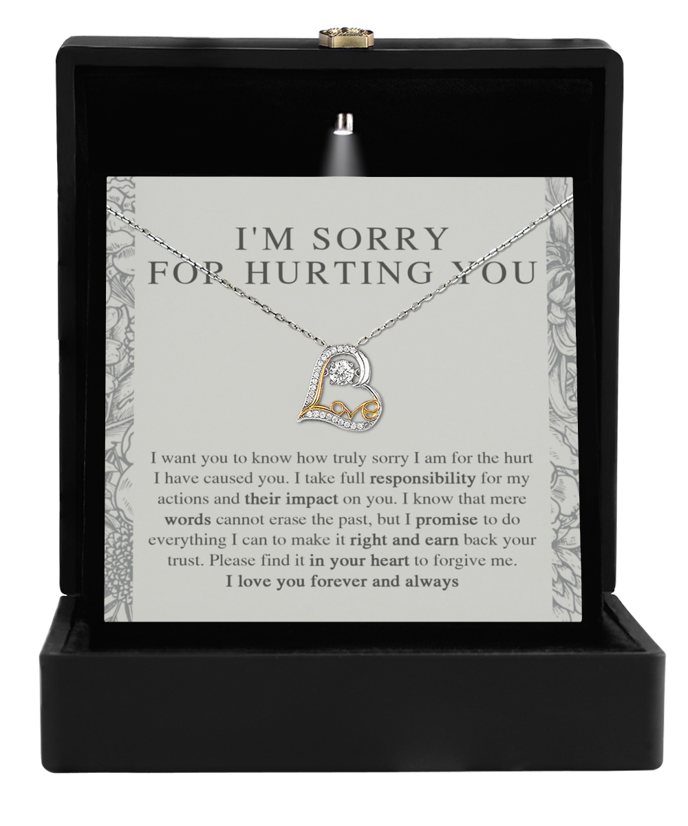 An open black jewelry box displaying the "Sorry-Do Everything - Love Dancing Necklace," featuring a sterling silver necklace with an intertwined heart pendant. Behind the necklace, a heartfelt apology note reads, "I'M SORRY FOR HURTING YOU," followed by a longer message expressing regret and a promise of love and reconciliation.