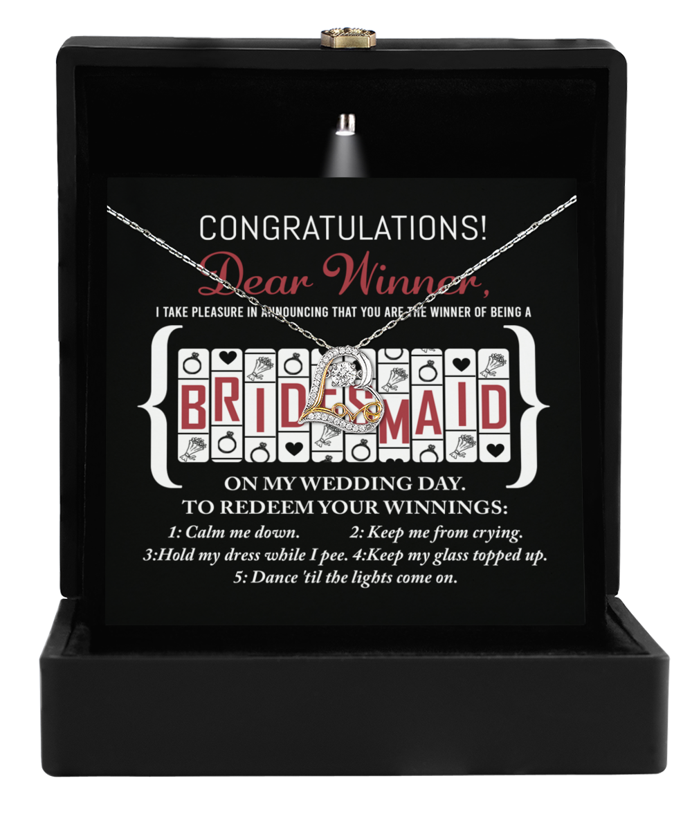 The "To Bridesmaid-The Winner Of - Love Dancing Necklace" features a black gift box with an interior light that illuminates the card and the sterling silver necklace inside. The card reads, "CONGRATULATIONS! Dear Winner, I take pleasure in announcing that you are the winner of being a Bridesmaid on my Wedding Day. To redeem your winnings..." followed by a list of five tasks.