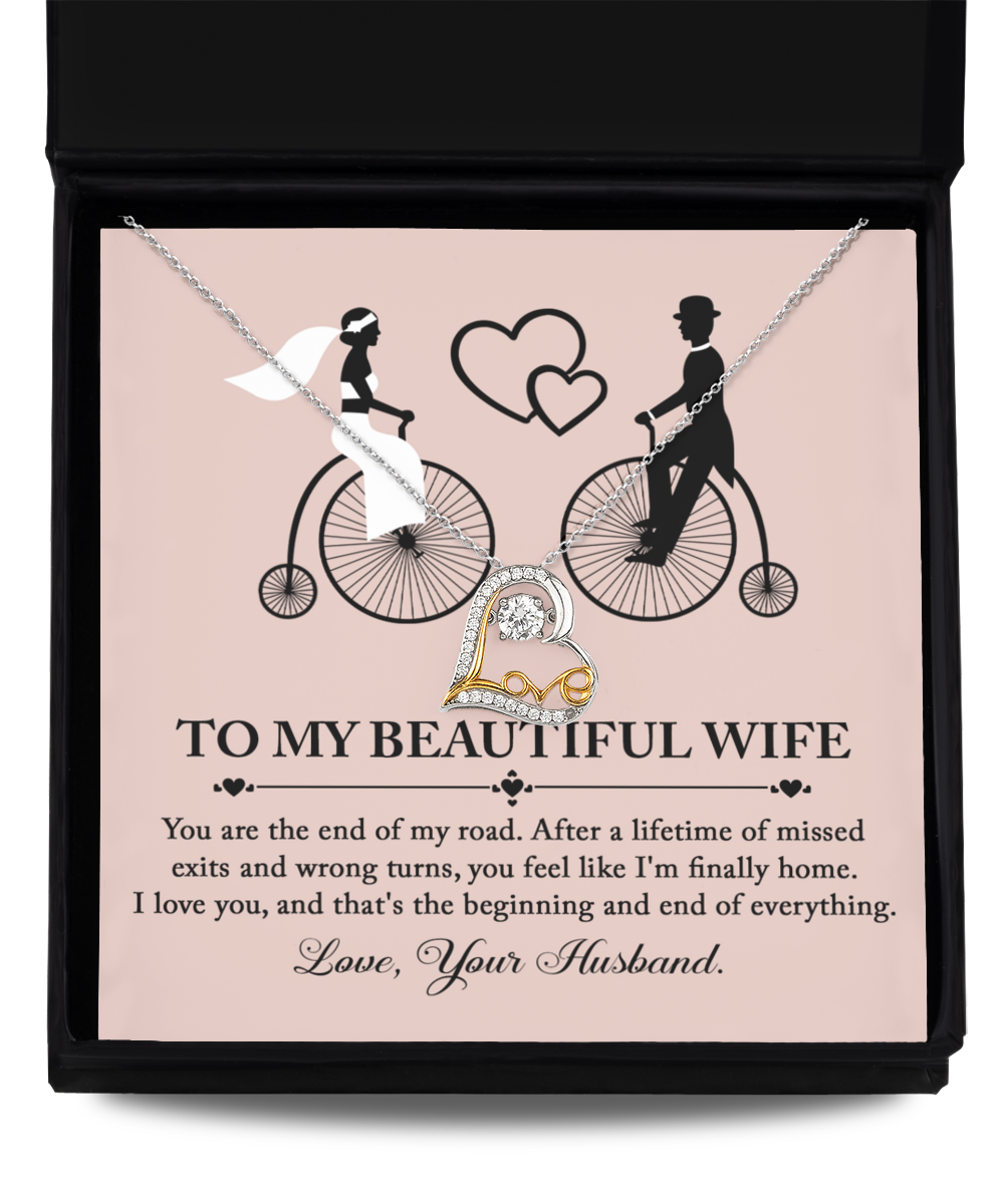 A beautiful To Wife, I'm Finally Home - Love Dancing Necklace in a box adorned with an illustration of a bride and groom on bicycles. The box, featuring the message "To My Beautiful Wife," expresses love and appreciation from "Your Husband." This necklace is crafted with .925 Sterling Silver, making it a timeless keepsake.