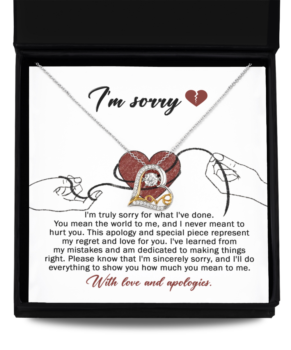 The "Sorry-Mean The World - Love Dancing Necklace," featuring a heart pendant, is displayed in a black box. The interior of the box is lined with 14k gold and includes an apology message expressing regret and love, along with an illustration of two hands holding red string.