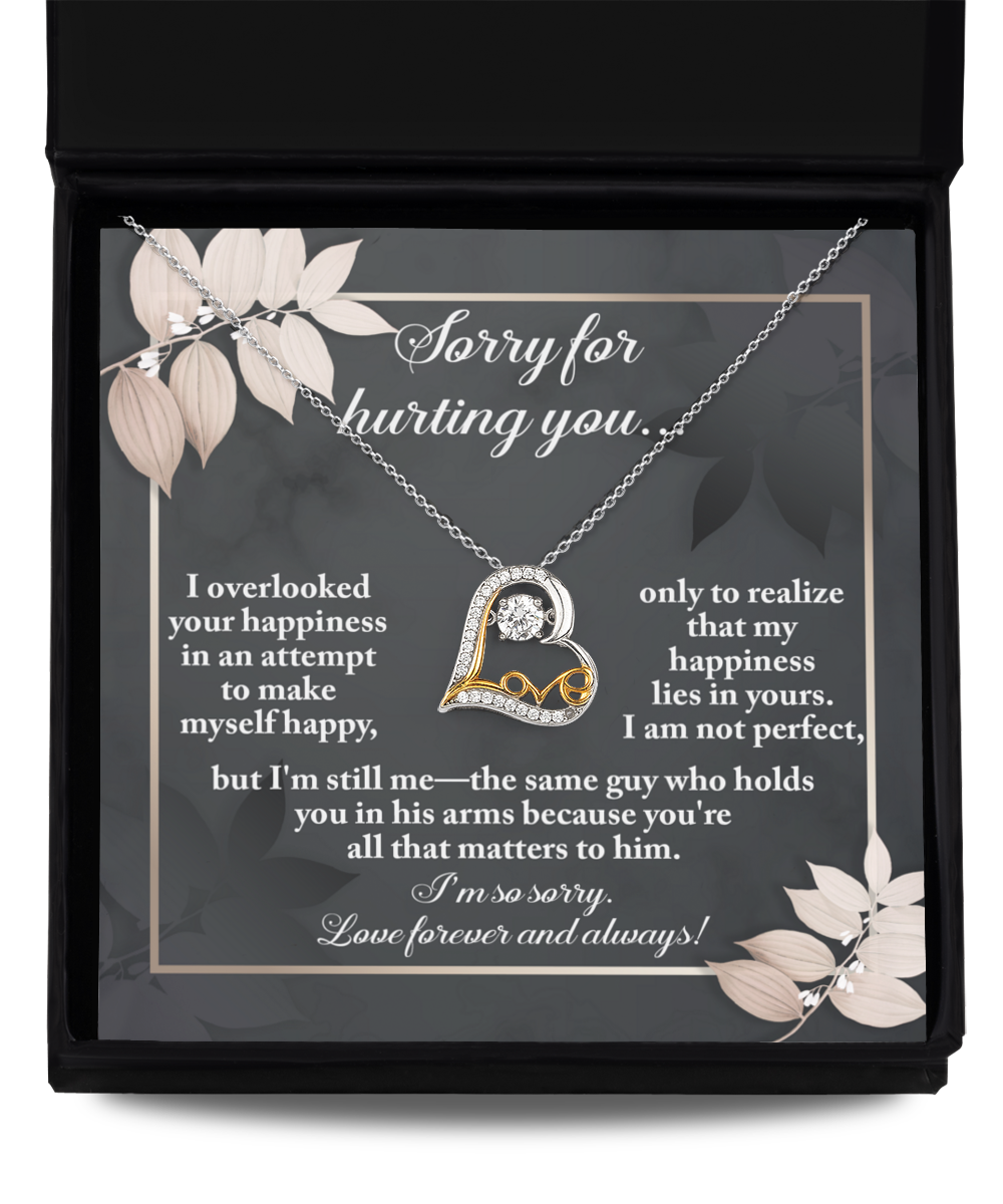 A heartfelt note within a black box accompanies the Sorry-Lies In Yours - Love Dancing Necklace, featuring a 14k gold loop enclosing a heart and a message apologizing for hurting the recipient while expressing enduring love and regret.