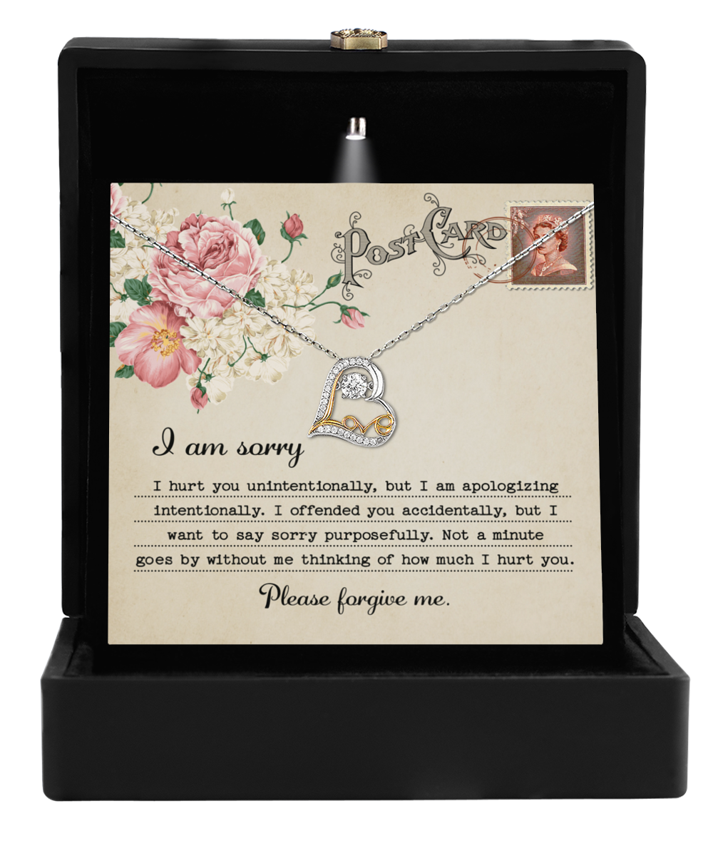 The Sorry-Apologizing Intentionally - Love Dancing Necklace showcases a silver heart elegantly suspended on a card adorned with an intricate floral design, all beautifully presented in a sleek black box. The apology text on the card conveys remorse and a deep yearning for forgiveness, symbolizing timeless maternal love.