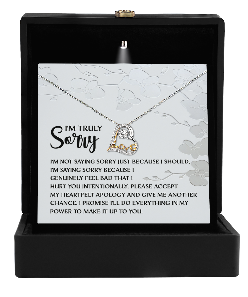 Inside an open black box is the Sorry-Feel Bad - Love Dancing Necklace, a 14k gold creation with a shimmering heart-shaped pendant. A card reads, "I'm Truly Sorry," accompanied by a heartfelt apology message.