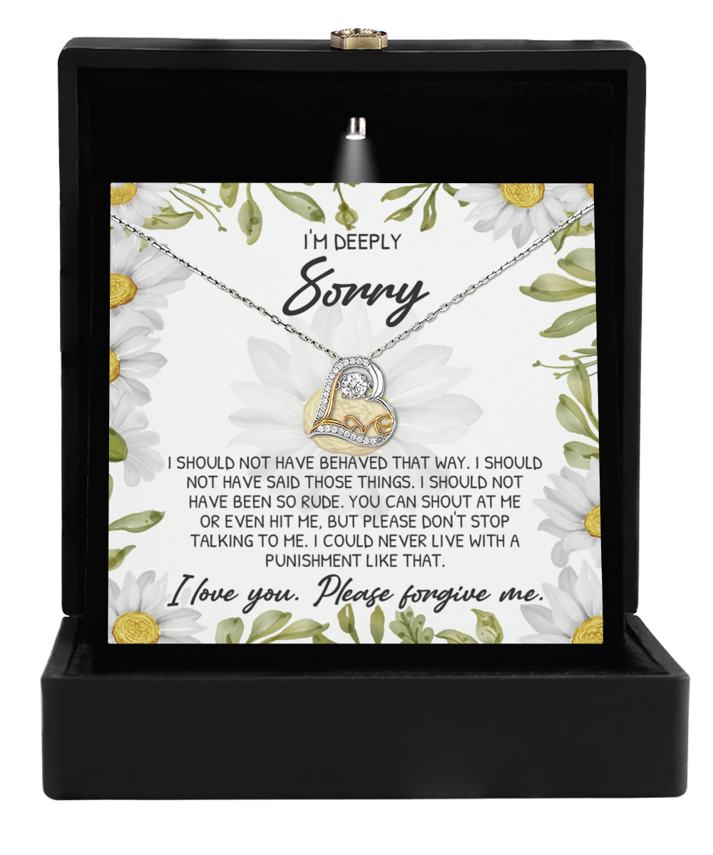 A "Sorry-Please Don't" Top - Love Dancing Necklace, featuring an intertwined heart pendant crafted in 14k gold, is displayed in an open black box adorned with daisy illustrations and a heartfelt apology message.