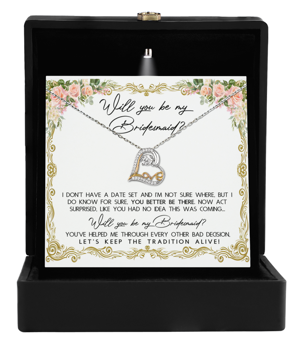 The Bridesmaid-Keep The Tradition - Love Dancing Necklace, featuring an elegant heart pendant, is showcased in an open black box along with a card that reads, "Will you be my bridesmaid?" Surrounded by beautiful floral designs, it makes the perfect bridesmaid gift.