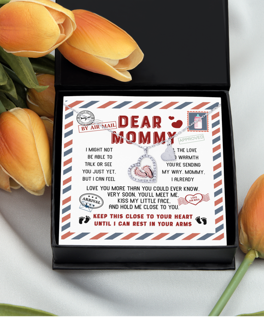 A gift box containing a personalized letter with "dear mommy" printed on it, flanked by orange tulips on a white background, includes a rose gold plated To Mommy, Little Face - Baby Feet Necklace.