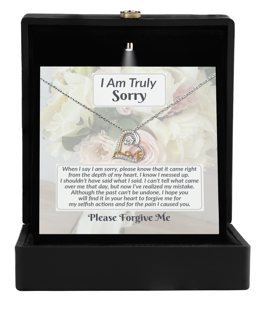 A heart-shaped sterling silver Sorry-What I Said - Love Dancing Necklace in a black box, accompanied by a note titled "I Am Truly Sorry" that expresses regret and seeks forgiveness, all set against an intricately detailed floral background.